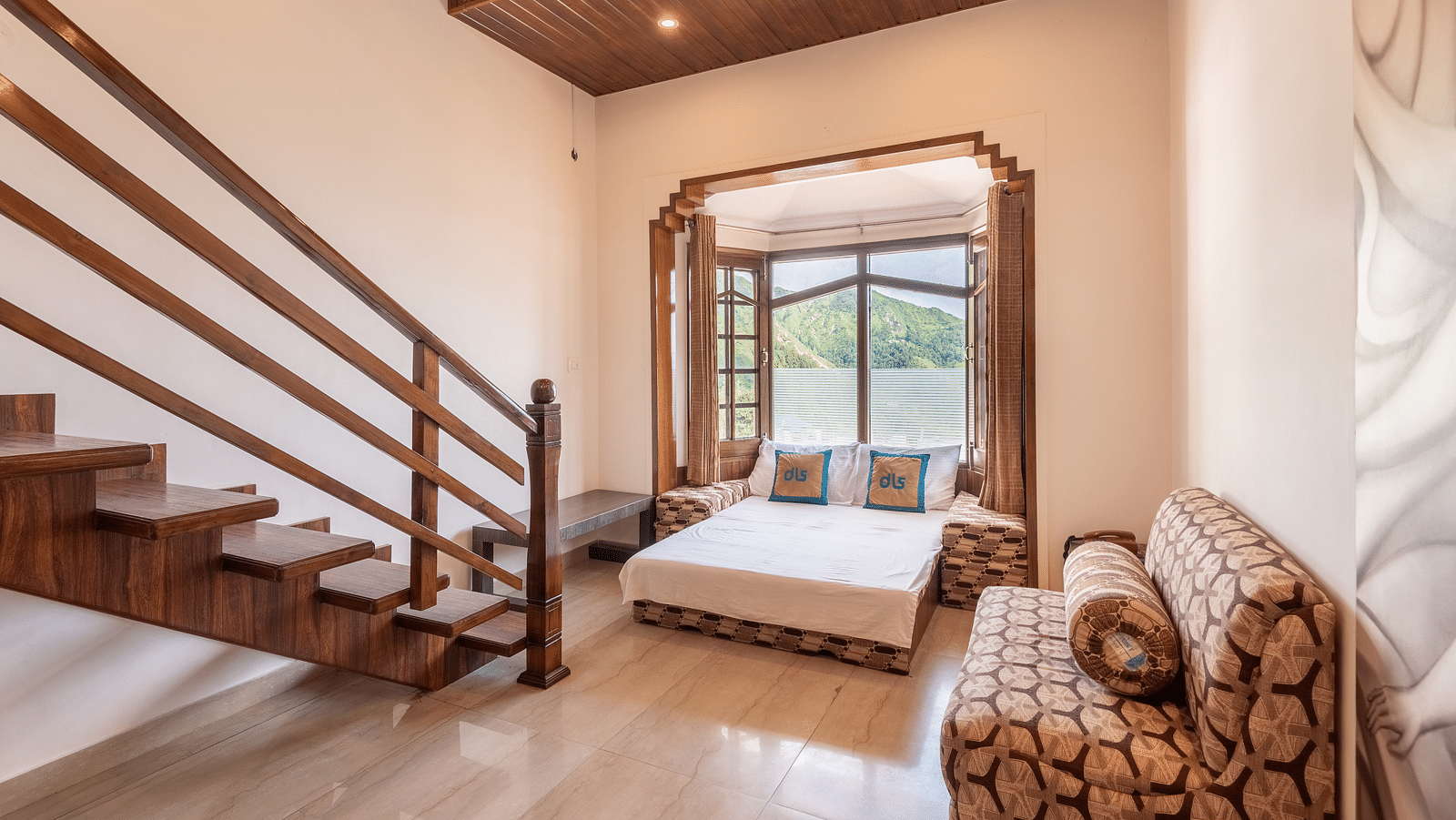 A spacious room near Bhagsunag Temple featuring a wooden staircase, a bed, a sofa, and a large window offering a mountain view – DLS Meghavan Resort.
